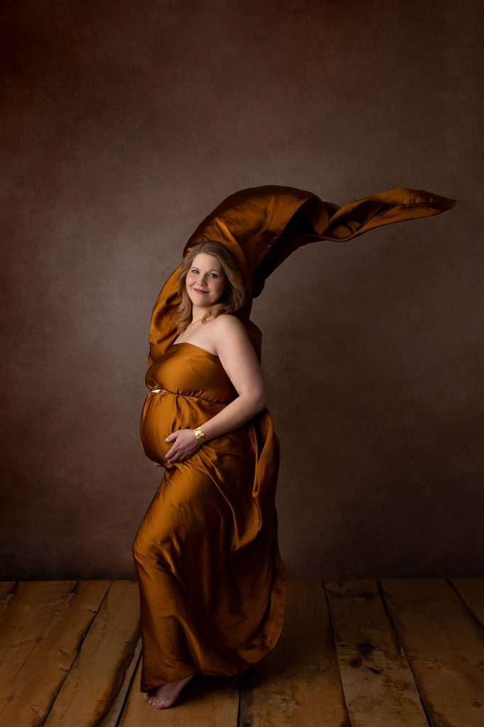 Schwangere Frau im goldenen Kleid, Stoff kunstvoll drapiert, Hochformat, Babybauchshooting bei Kahle Fotografie